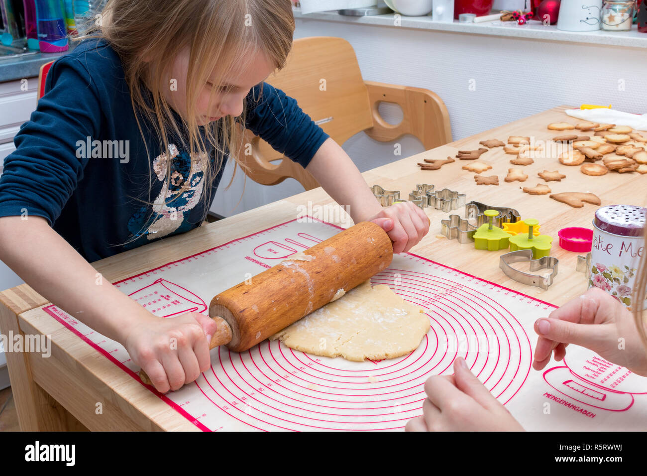 A girl is using the pastry roller to roll out the dough on the table Stock Photo