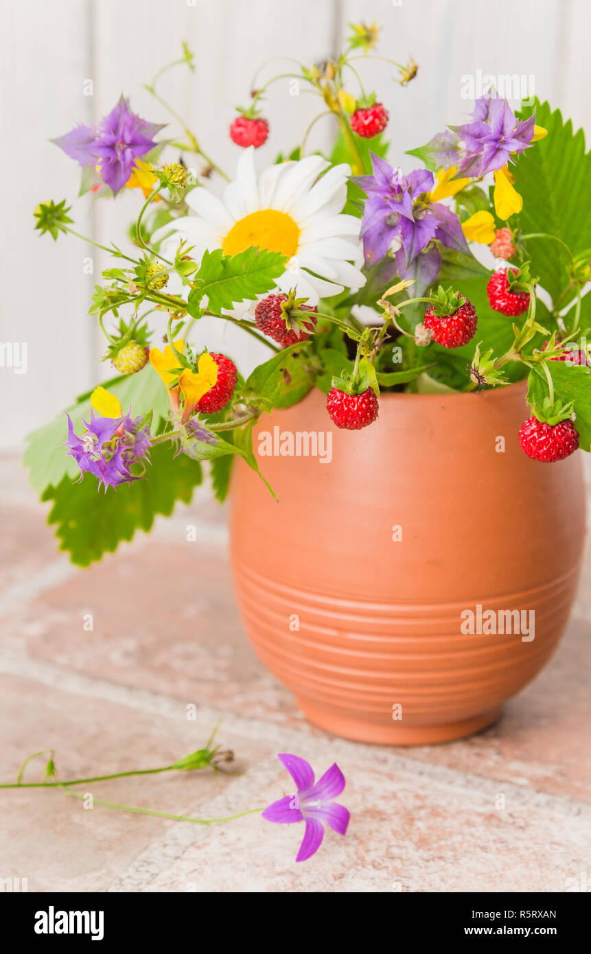 Ripe strawberries and a bouquet of forest flowers in a clay mug Stock Photo