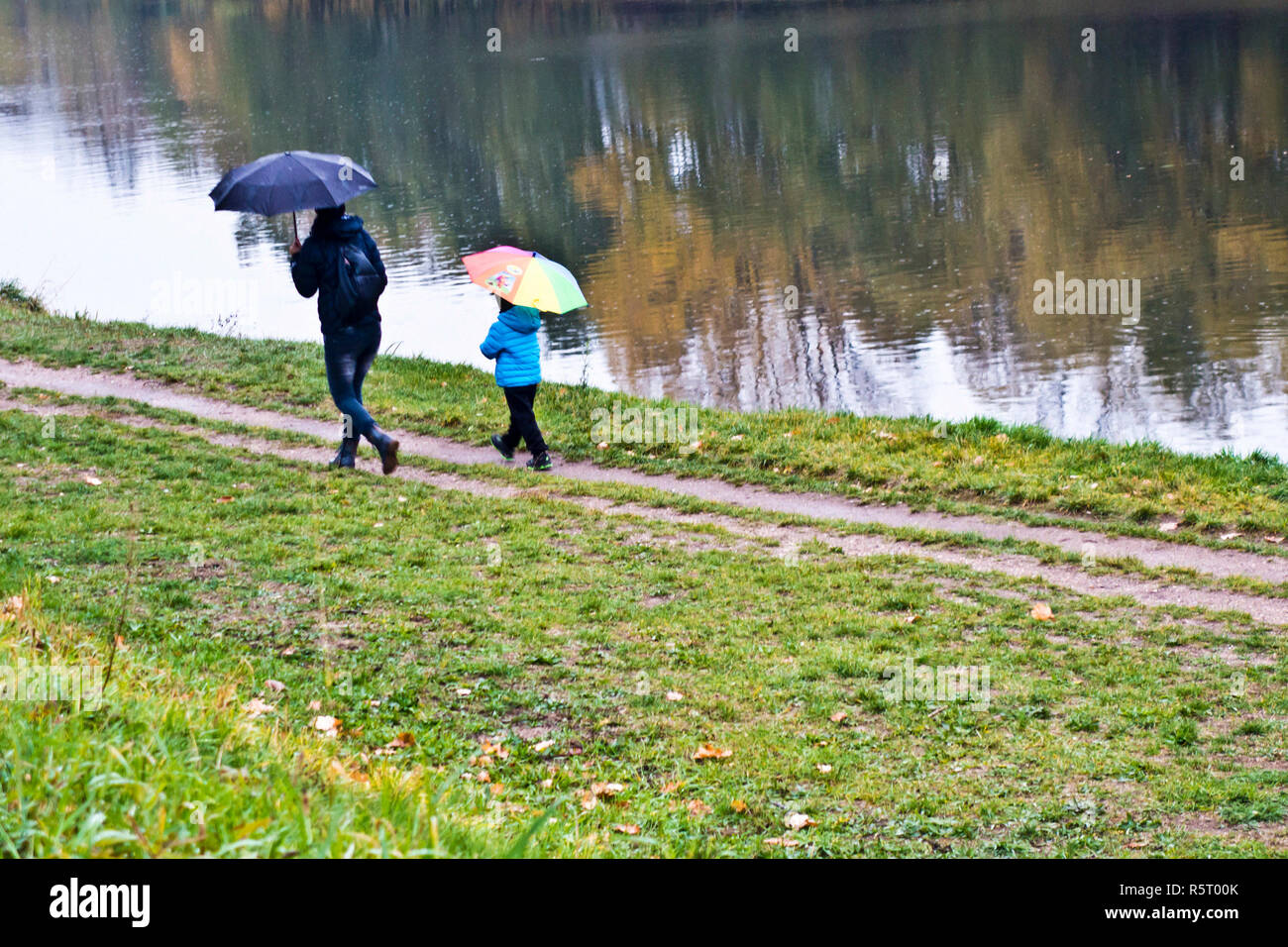 mother with her child walking along a river with umbrellas in a rainy day Stock Photo