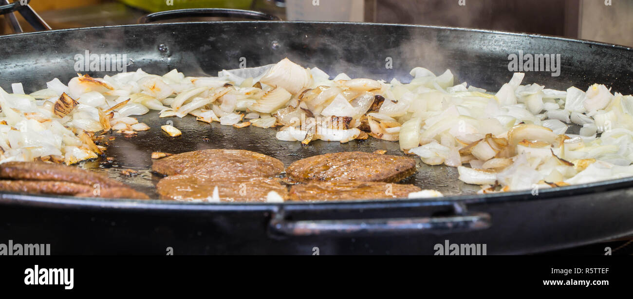 Lamb burgers and onions cooking in large frying pan. Victorian