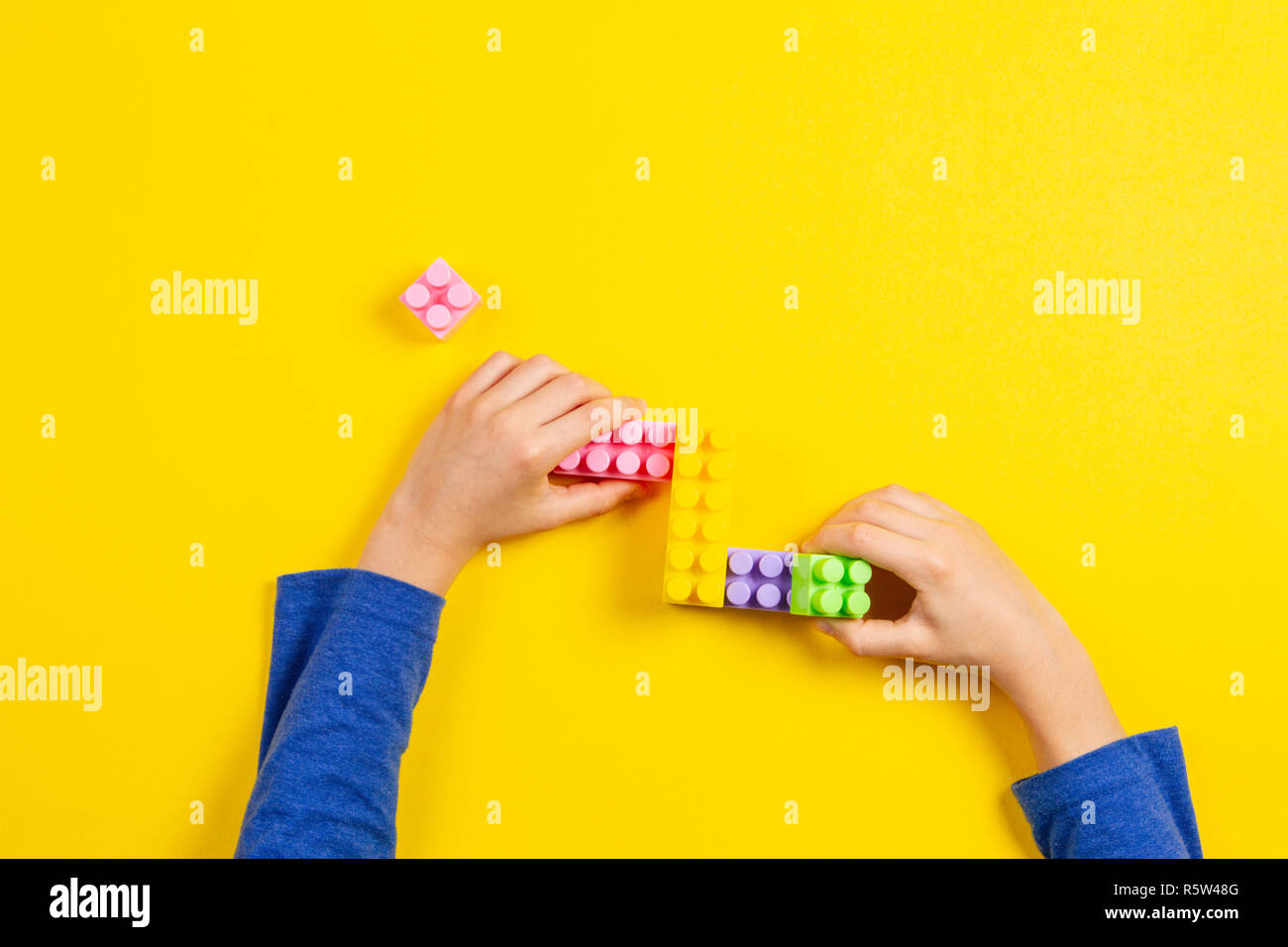 Kid hands playing with colorful plastic bricks on yellow background ...
