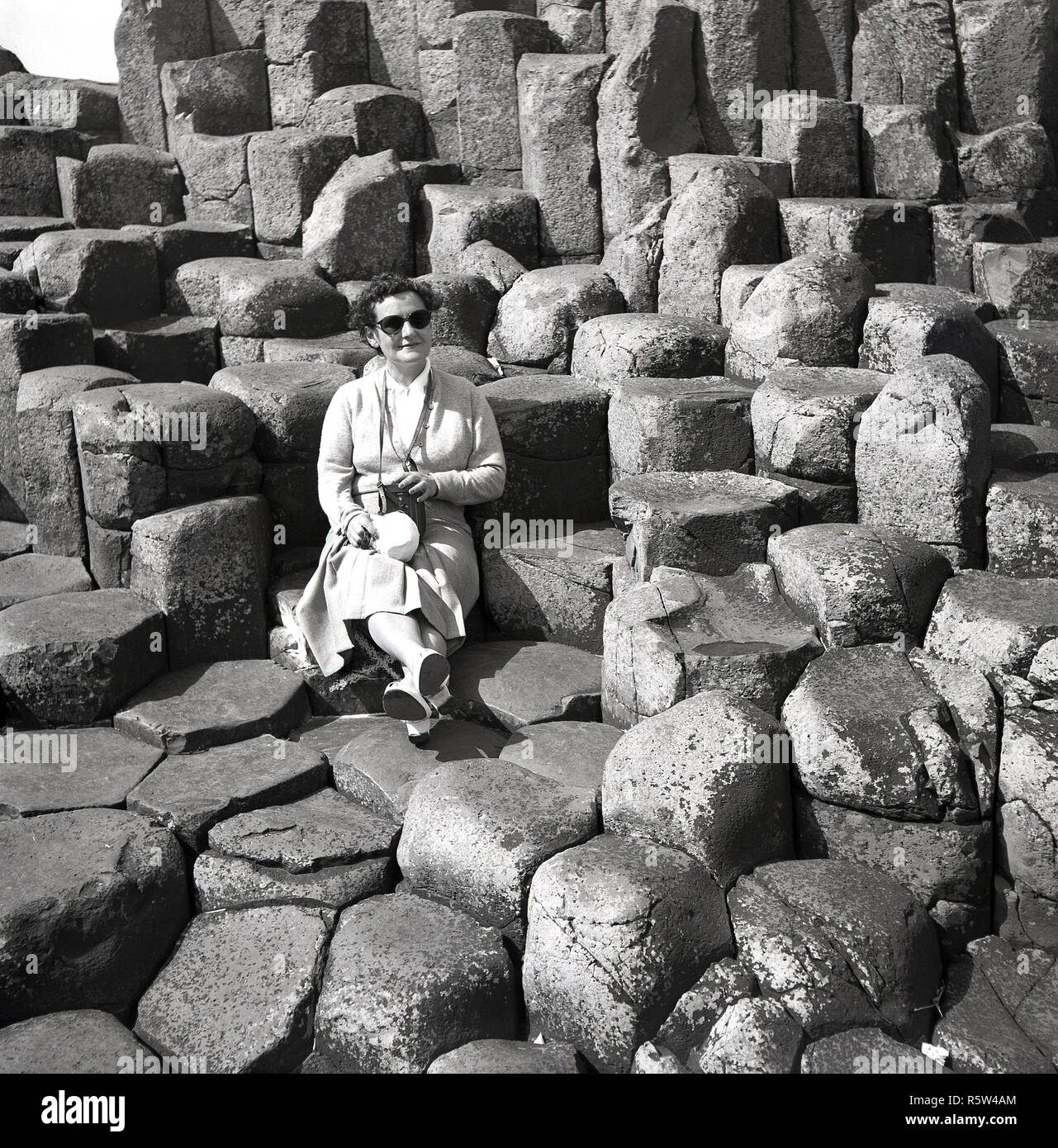 1950s, historical, a lady sitting on the ancient volcanic basalt columns at the Giant's Causeway in Co. Antrim, Northern Ireland. At the North Atlantic coast, the causeway is a geological wonder, an area of 40,000 interlocking basalt stone columns, the result of an ancient volcanic fissure eruption. Stock Photo