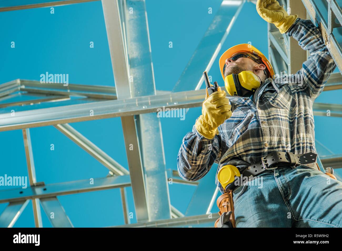 Construction Worker on Duty. Caucasian Contractor with Walkie Talkie and the Skeleton Steel Project. Industrial Site. Stock Photo