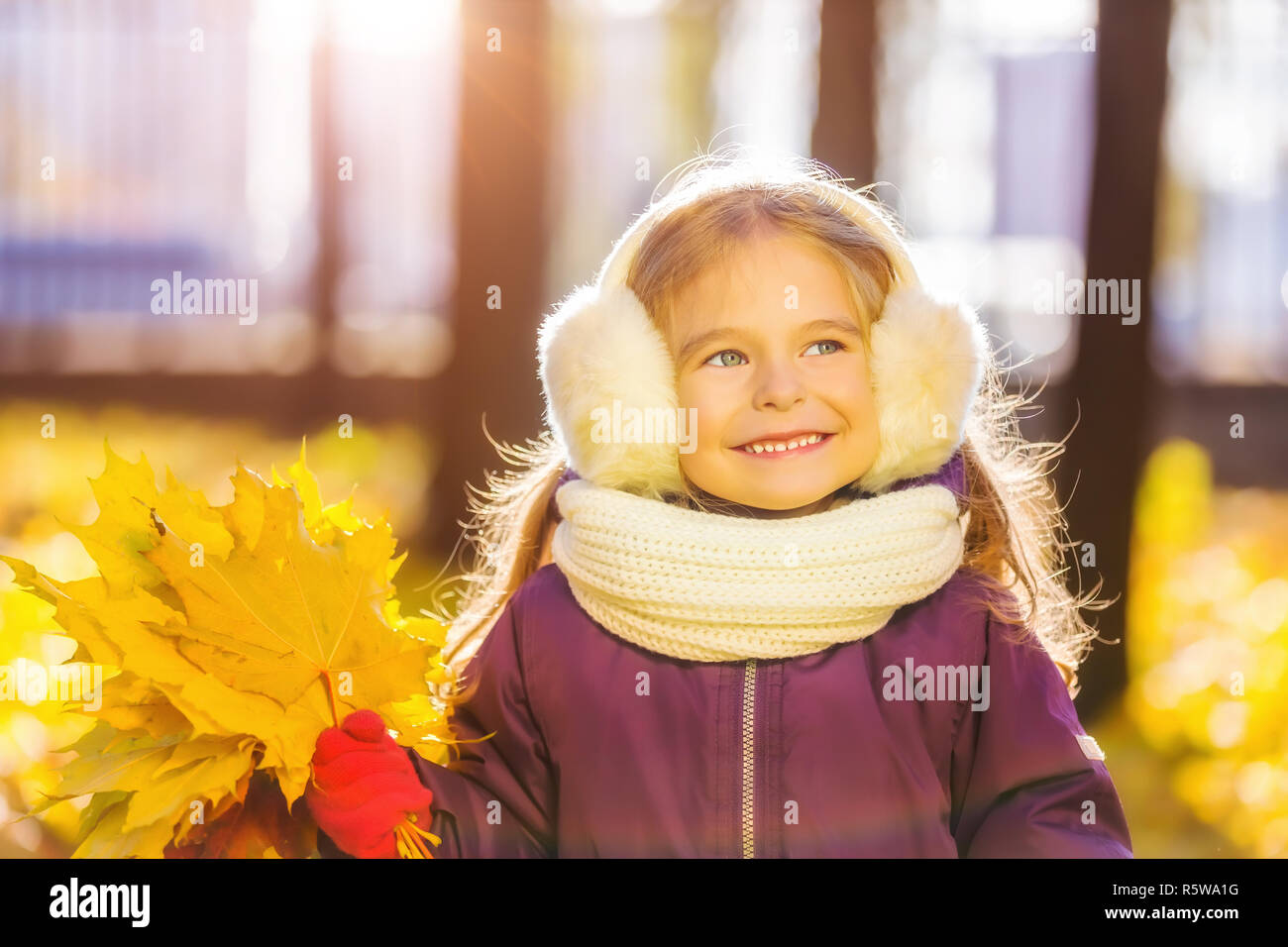 Happy little girl in earflaps with autumn leaves Stock Photo