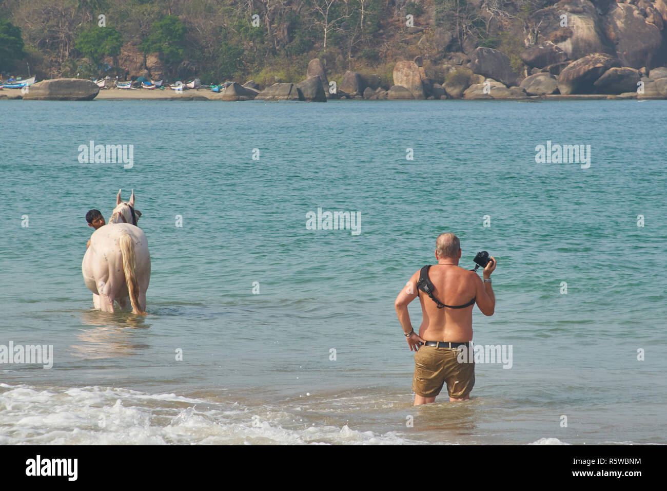A tourist taking a picture of a man washing his horse in the Arabian sea Stock Photo