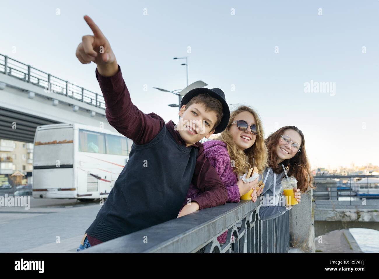 Lifestyle of adolescents, boy and two teen girls are walking in the city. Laughing, talking children eating street food, having fun. Background of the Stock Photo