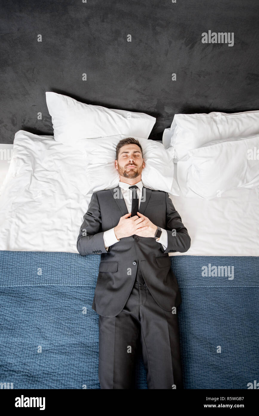 Businessman in the suit lying on the bed like a dead man at the hotel room or bedroom Stock