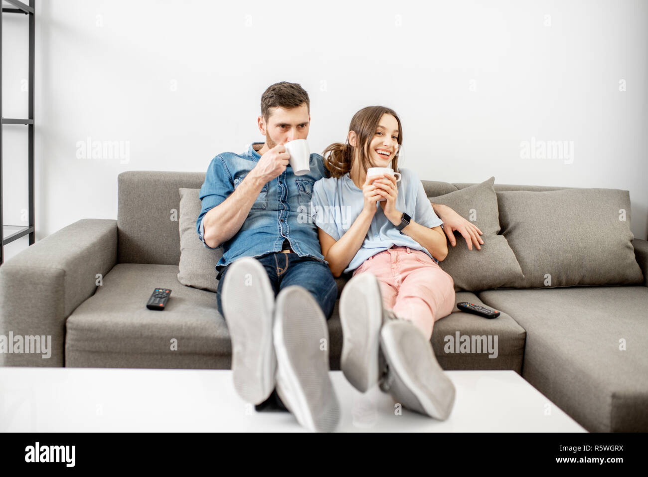 Young couple dressed casually sitting together on the couch and watching TV at home Stock Photo