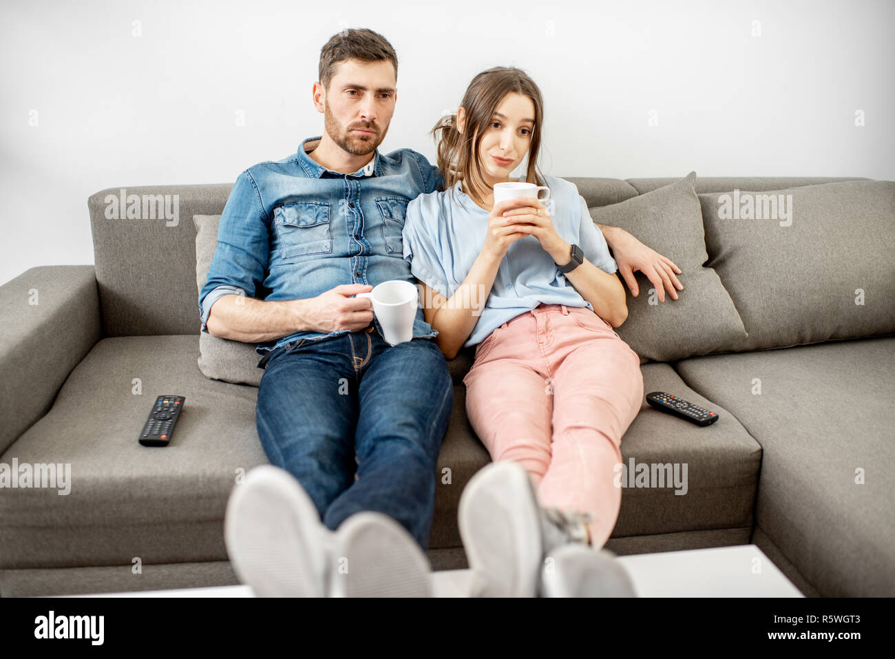 Young Couple With Unhappy Faces Watching Boring Tv Sitting Together On