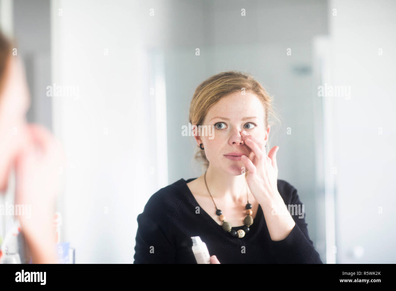 Woman standing in bathroom applying make-up Stock Photo