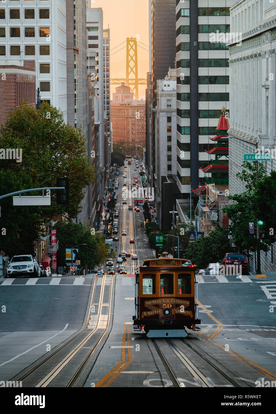Looking down a steep hill at the California Line Cable Car with the San Francisco Bay Bridge in the distance Stock Photo