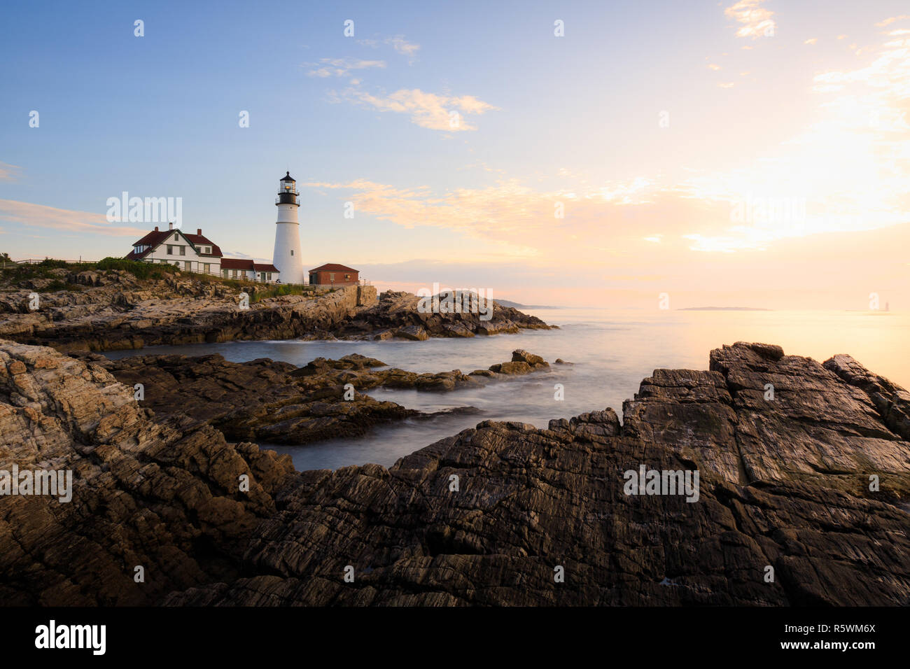 Portland Head Light in Fort Williams Park during a beautiful sunrise with the rocky coast in the foreground and ocean in mid and background in Maine Stock Photo