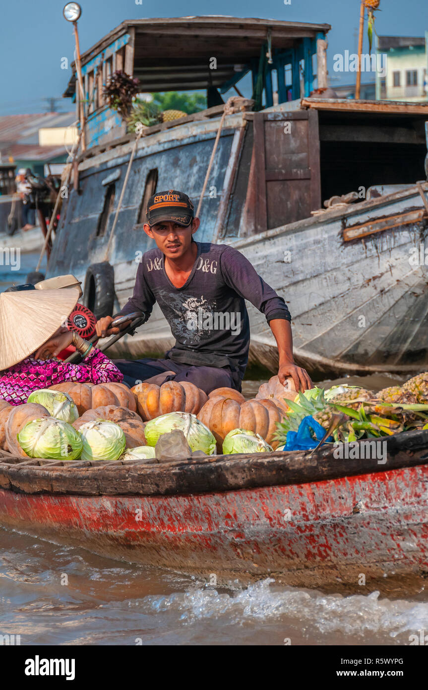 Boatman in wooden boat loaded with fruit and vegetables steers through the chaos of the Cai Rang Floating Market, Can Tho Province,Vietnam Stock Photo