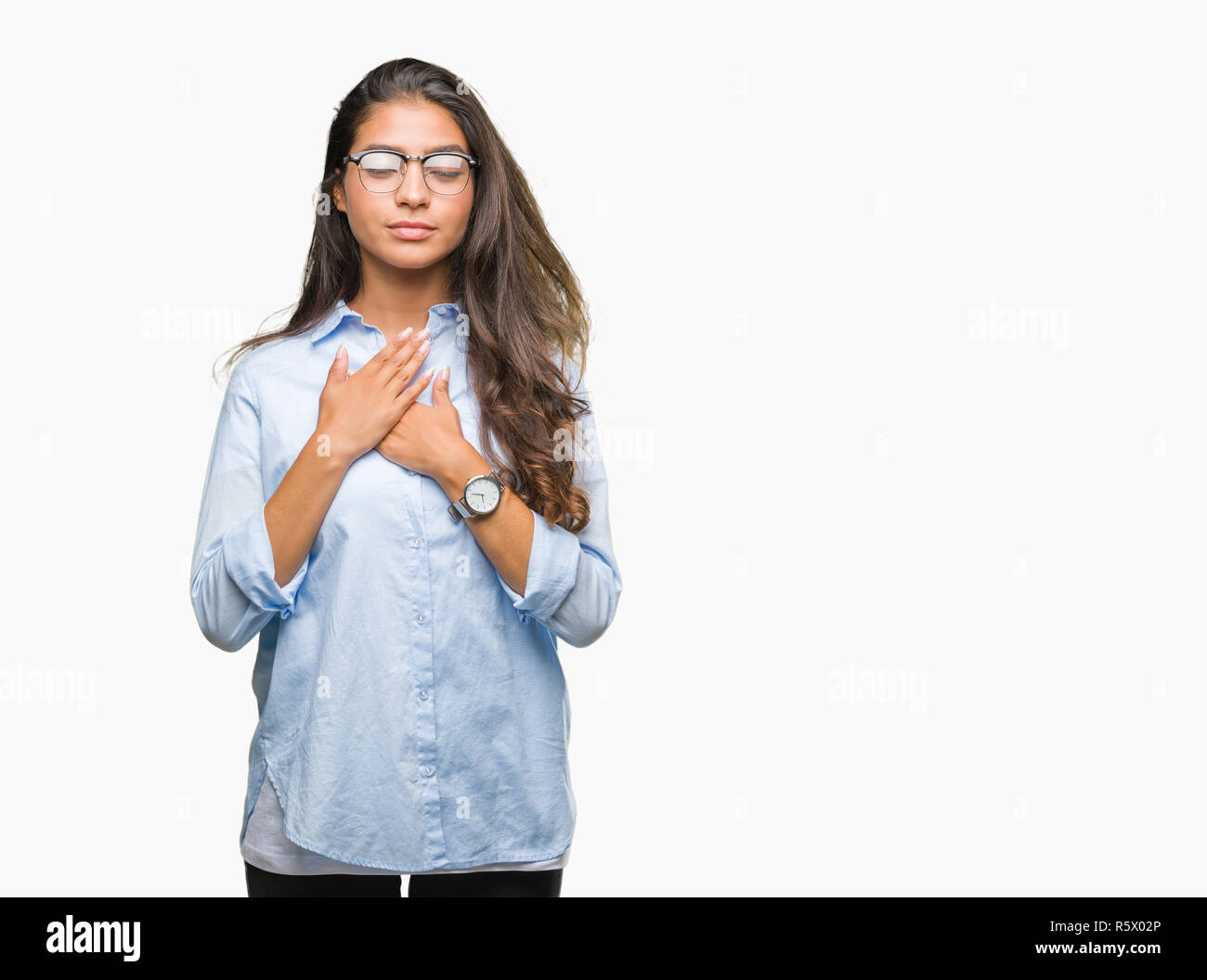 Young beautiful arab woman wearing glasses over isolated background smiling with hands on chest with closed eyes and grateful gesture on face. Health  Stock Photo
