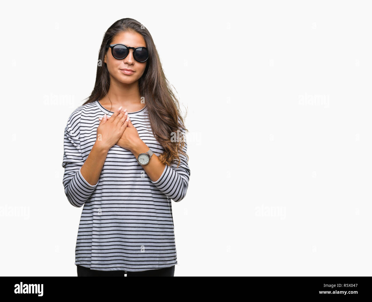 Young beautiful arab woman wearing sunglasses over isolated background smiling with hands on chest with closed eyes and grateful gesture on face. Heal Stock Photo