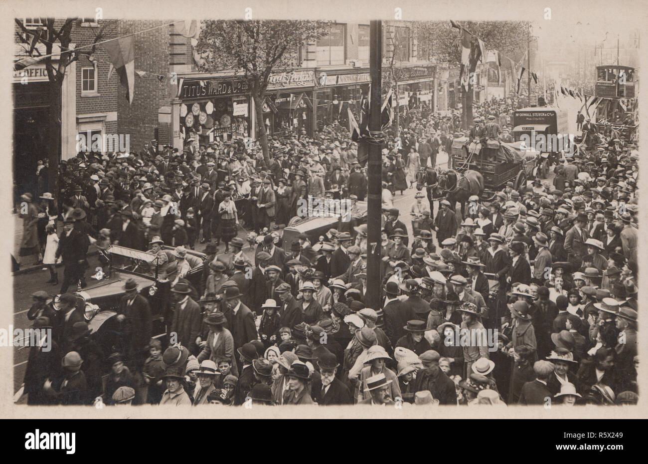 Vintage British Photographic Postcard Showing a Large Public Event With a Procession of Automobiles and Horse Drawn Vehicles. One of The Visible Shops is Titus Ward & Co Ltd. One of The Vehicles Has a Sign For McDowall Steven & Co Ltd. Stock Photo