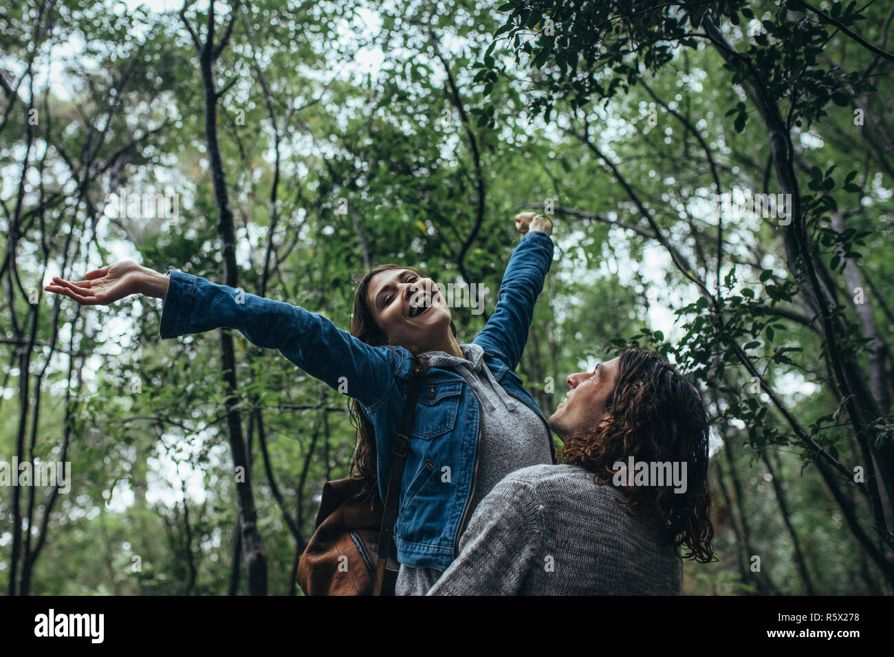 Young woman with her boyfriend in a forest having a great time. Man carrying his girlfriend with arms outstretched and enjoying the rain. Stock Photo