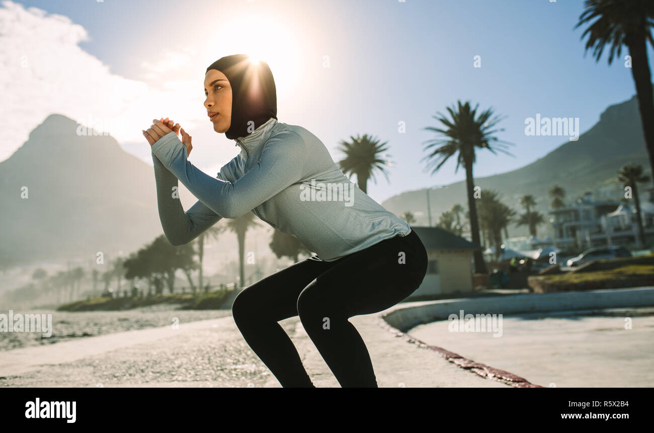 Fit woman doing squats outdoors in morning. Hijab girl exercising in the city in morning. Stock Photo