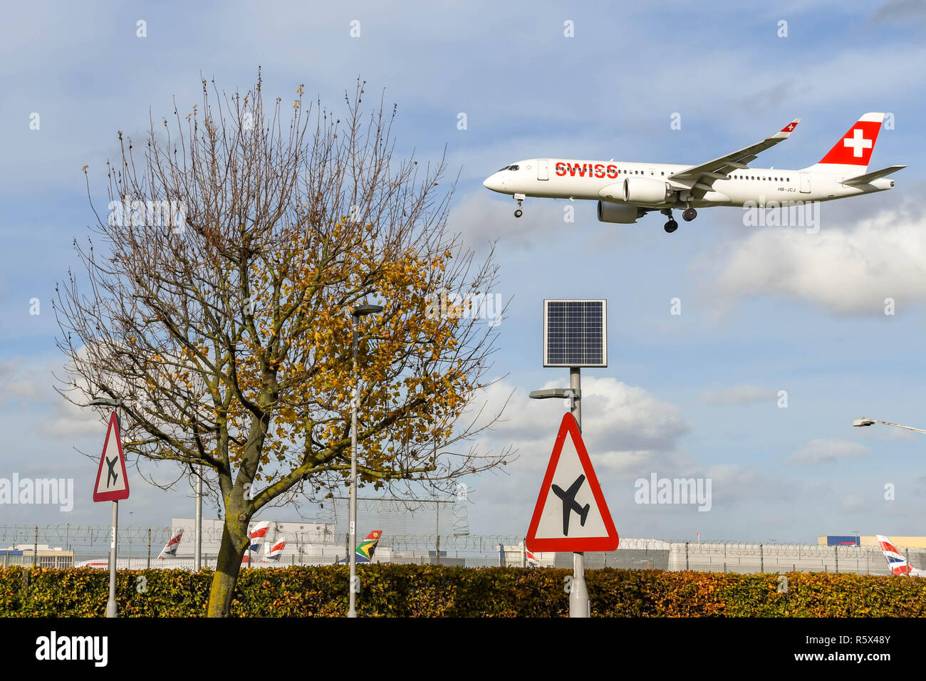 LONDON, ENGLAND - NOVEMBER 2018: Road sign on the A30 road at London Heathrow Airport warning motorists of low flying aircarft. A Swiss airlines jet i Stock Photo