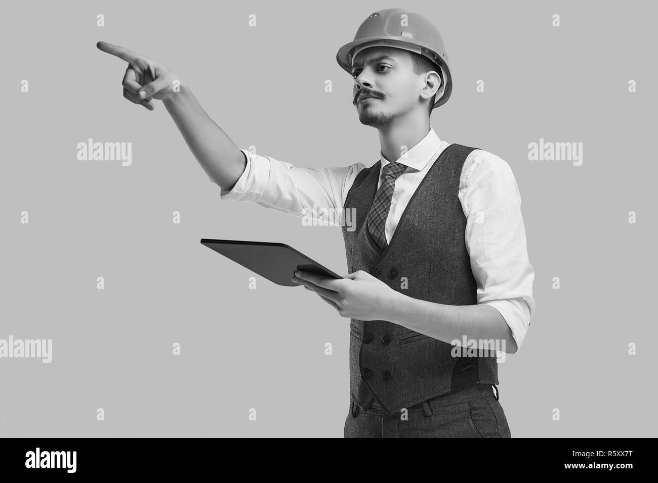 Portrait of handsome young confident arabic architect with fancy mustache in woolen suit and construction helmet holds tablet Stock Photo