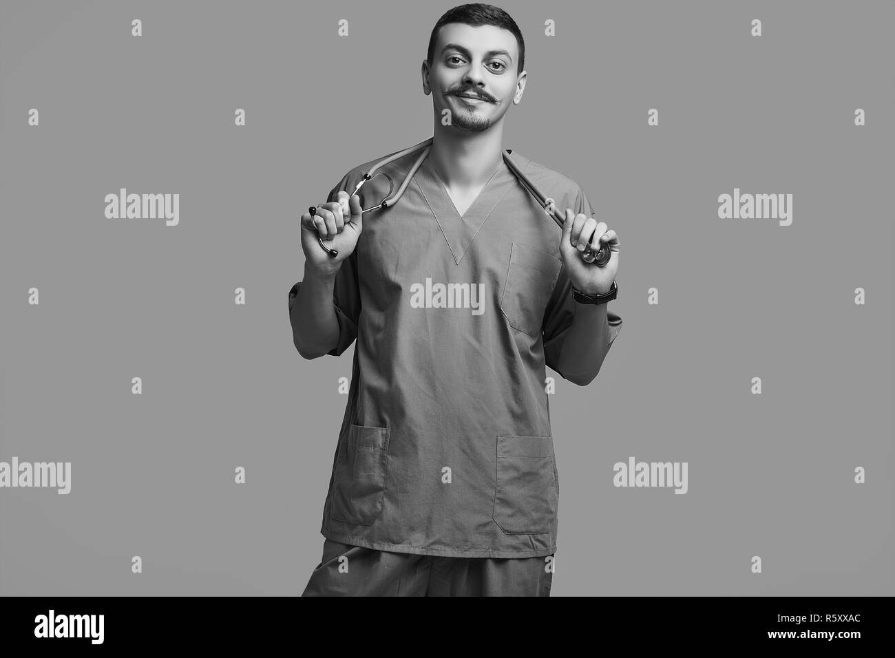 Portrait of handsome young confident arabic doctor with fancy mustache in blue on gray studio background Stock Photo