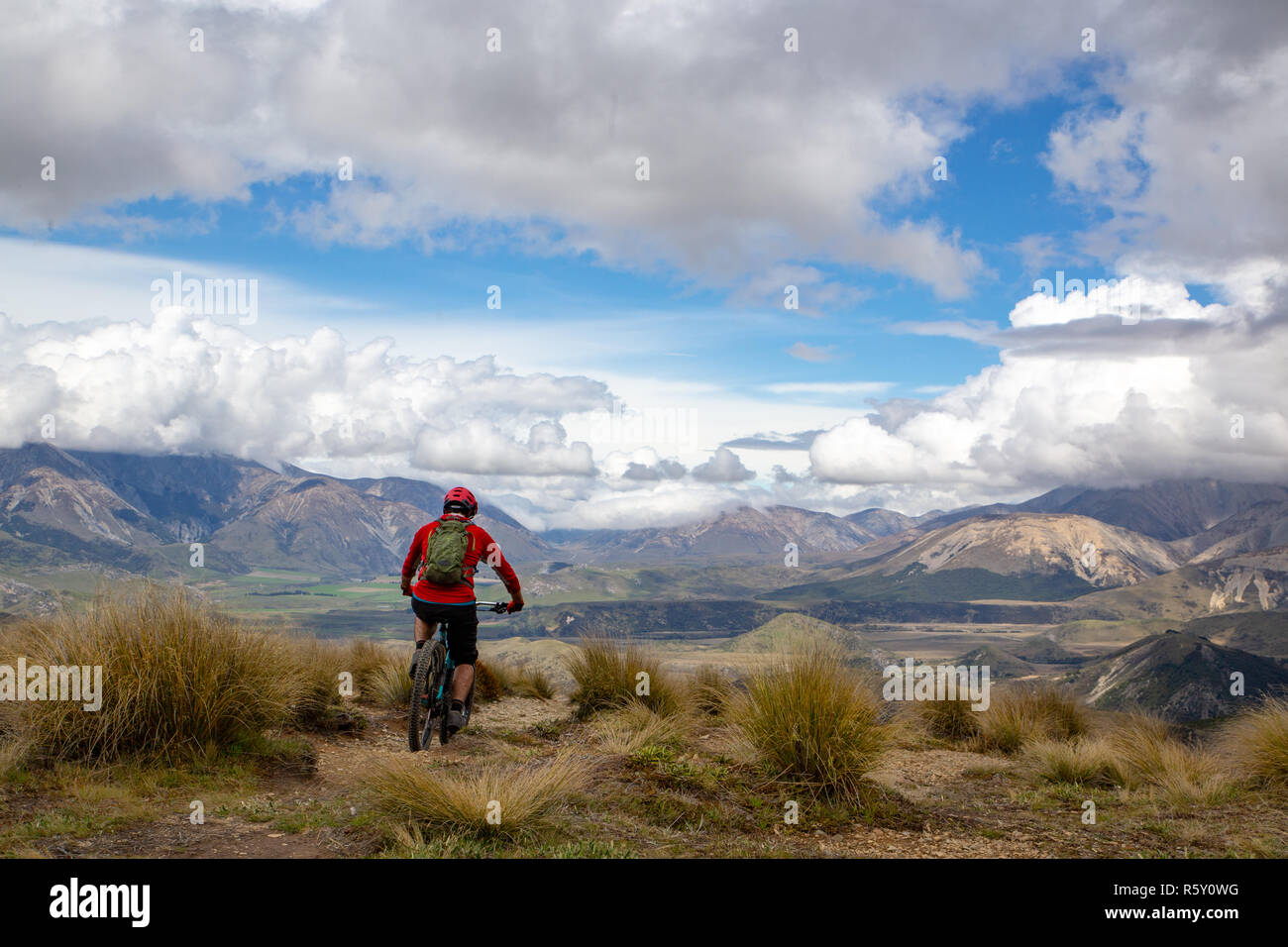 A mountain biker rides along the ridge and descends the mountain with beautiful scenery way down below Stock Photo