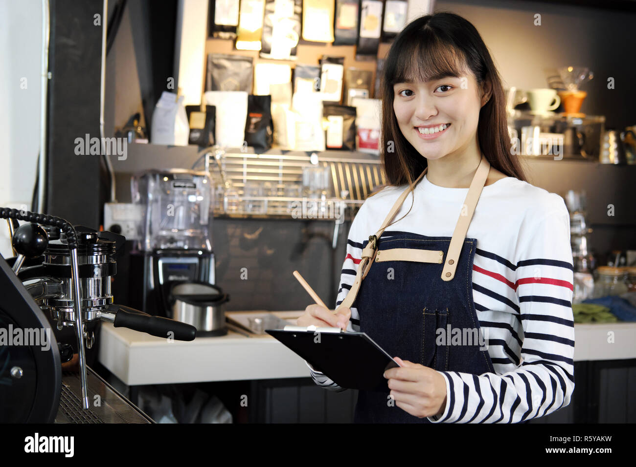 Portrait of smiling asian barista listing food. Cafe restaurant service, food and drink industry concept. Stock Photo