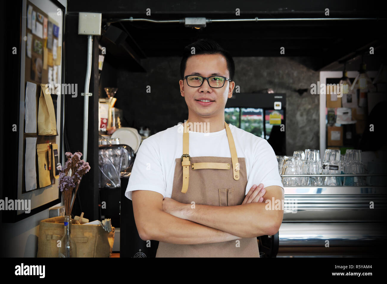Portrait of smiling asian barista with arms crossed at counter in coffee shop. Cafe restaurant service, food and drink industry concept. Stock Photo