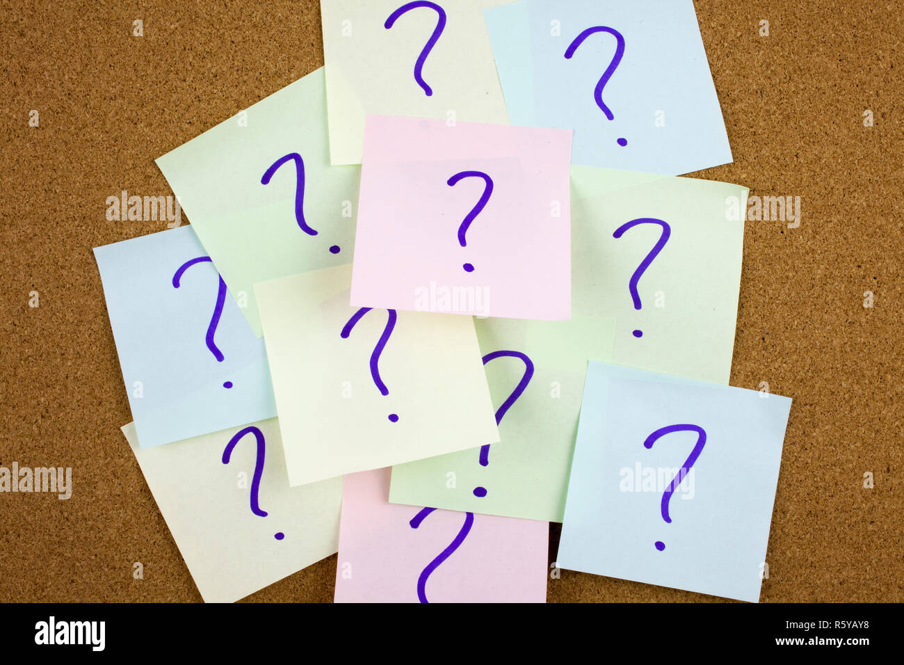 A yellow sticky note writing, caption, inscription Pile of colorful paper notes with question marks. Closeup. Stock Photo