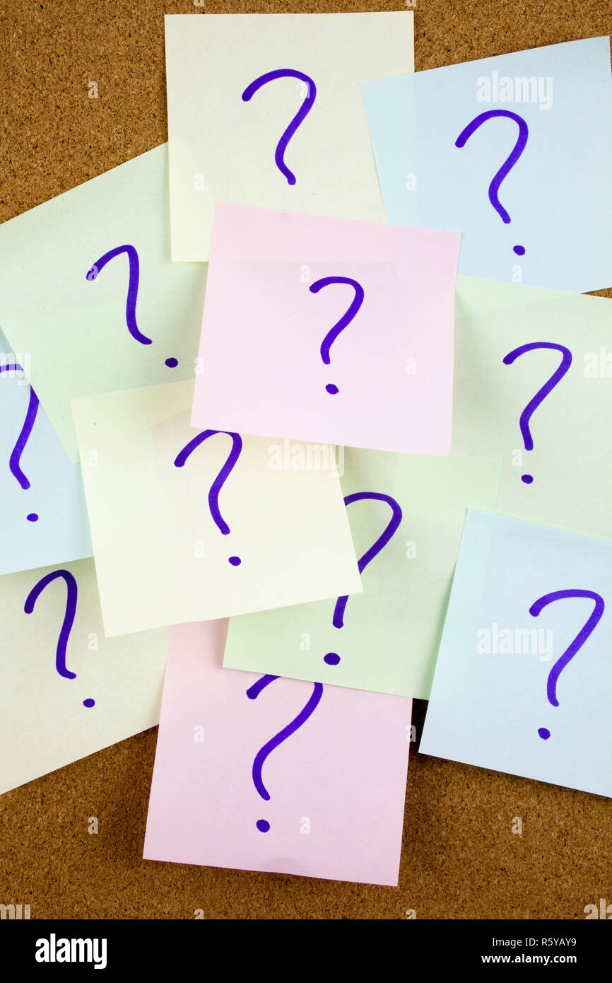 A yellow sticky note writing, caption, inscription Pile of colorful paper notes with question marks. Closeup. Stock Photo