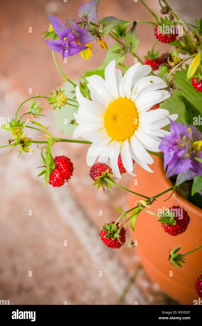 Ripe strawberries and a bouquet of forest flowers in a clay mug Stock Photo