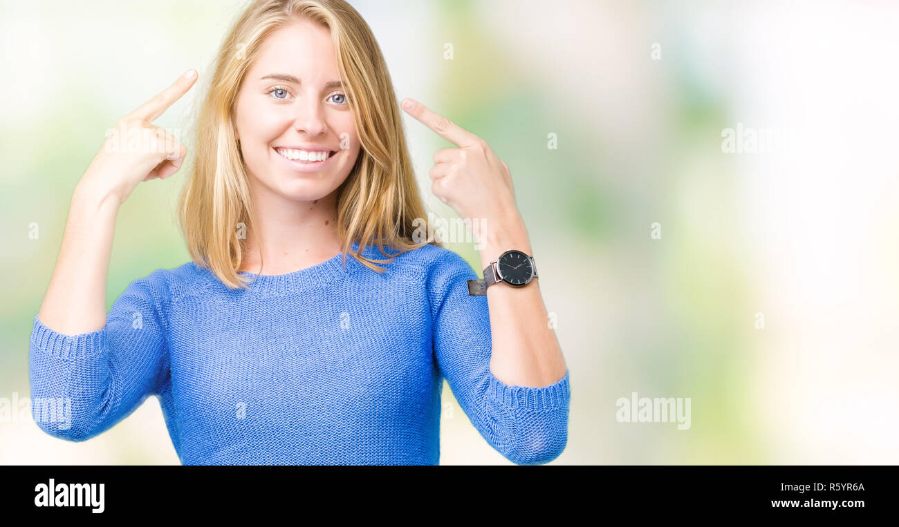 Beautiful young woman wearing blue sweater over isolated background Smiling pointing to head with both hands finger, great idea or thought, good memor Stock Photo