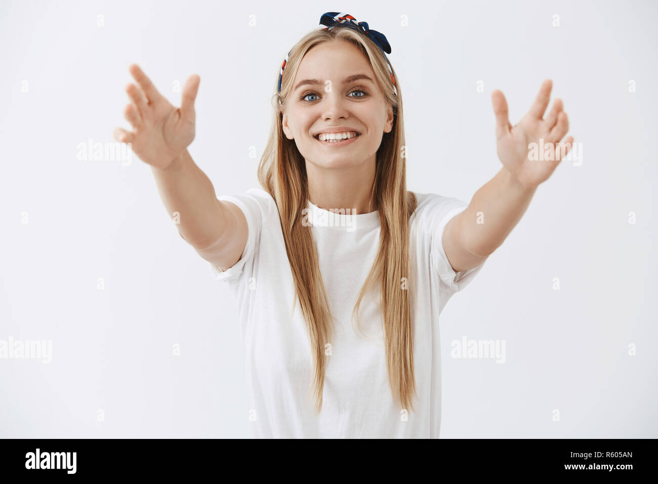 Come to me in my arms cutie. Portrait of tender attractive and joyful young woman with fair hair in headband pulling hands towards camera to give warm Stock Photo