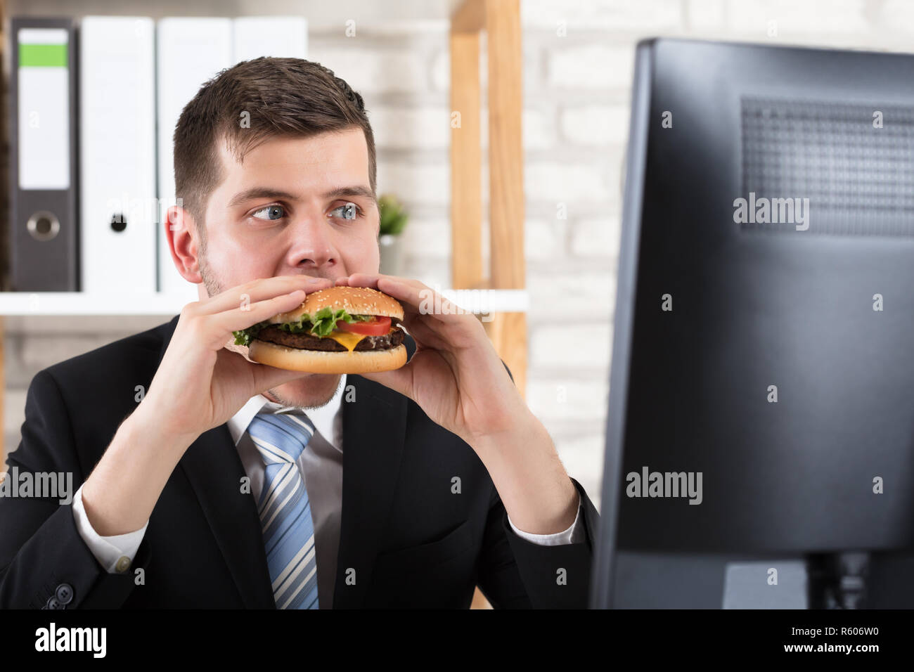 Business Man Eating Burger While Looking At Computer Stock Photo