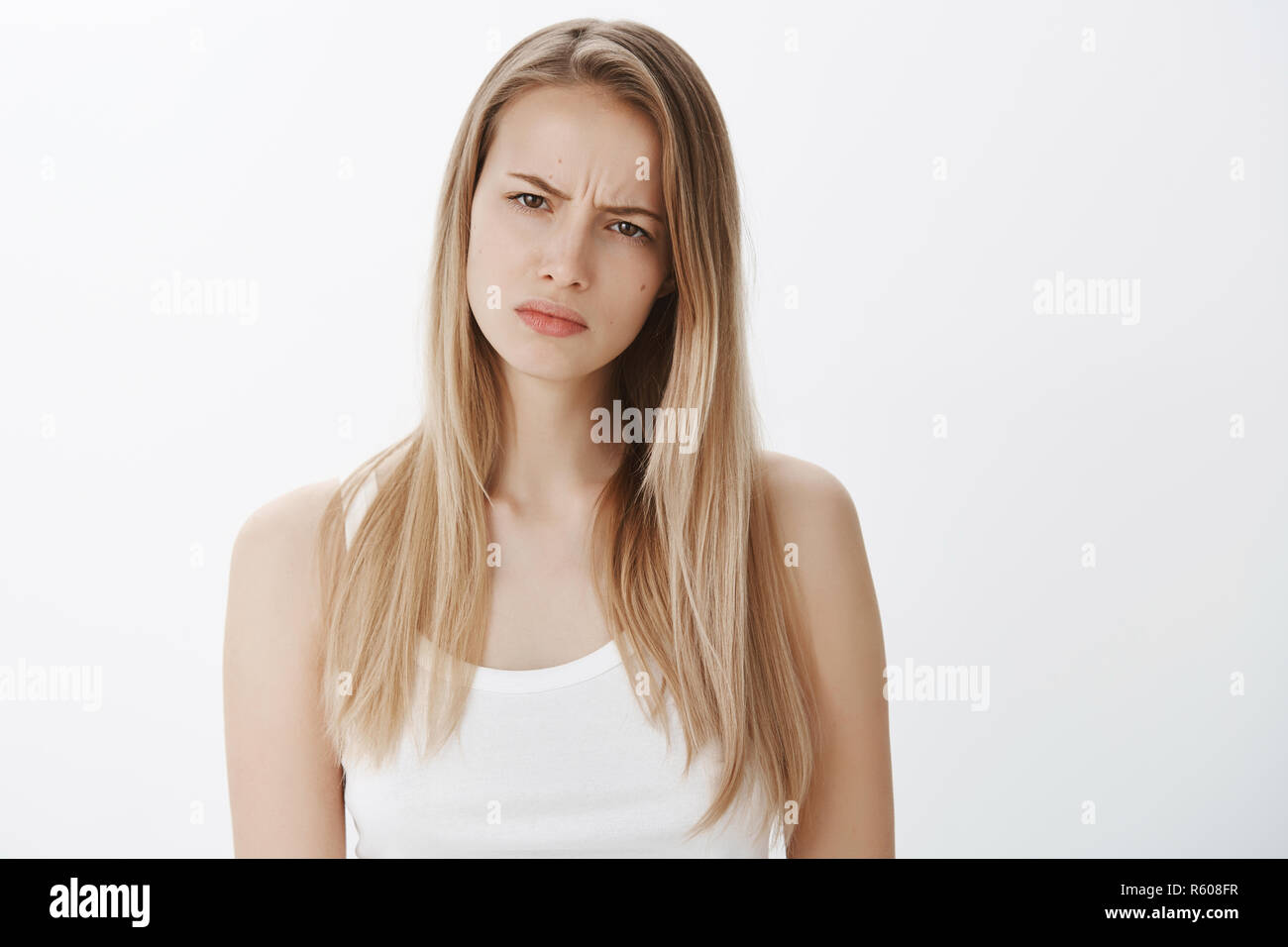 Girl suspects something wrong being doubtful in friend telling whole truth, squinting suspicious at camera as frowning and making hesitant face, stand Stock Photo