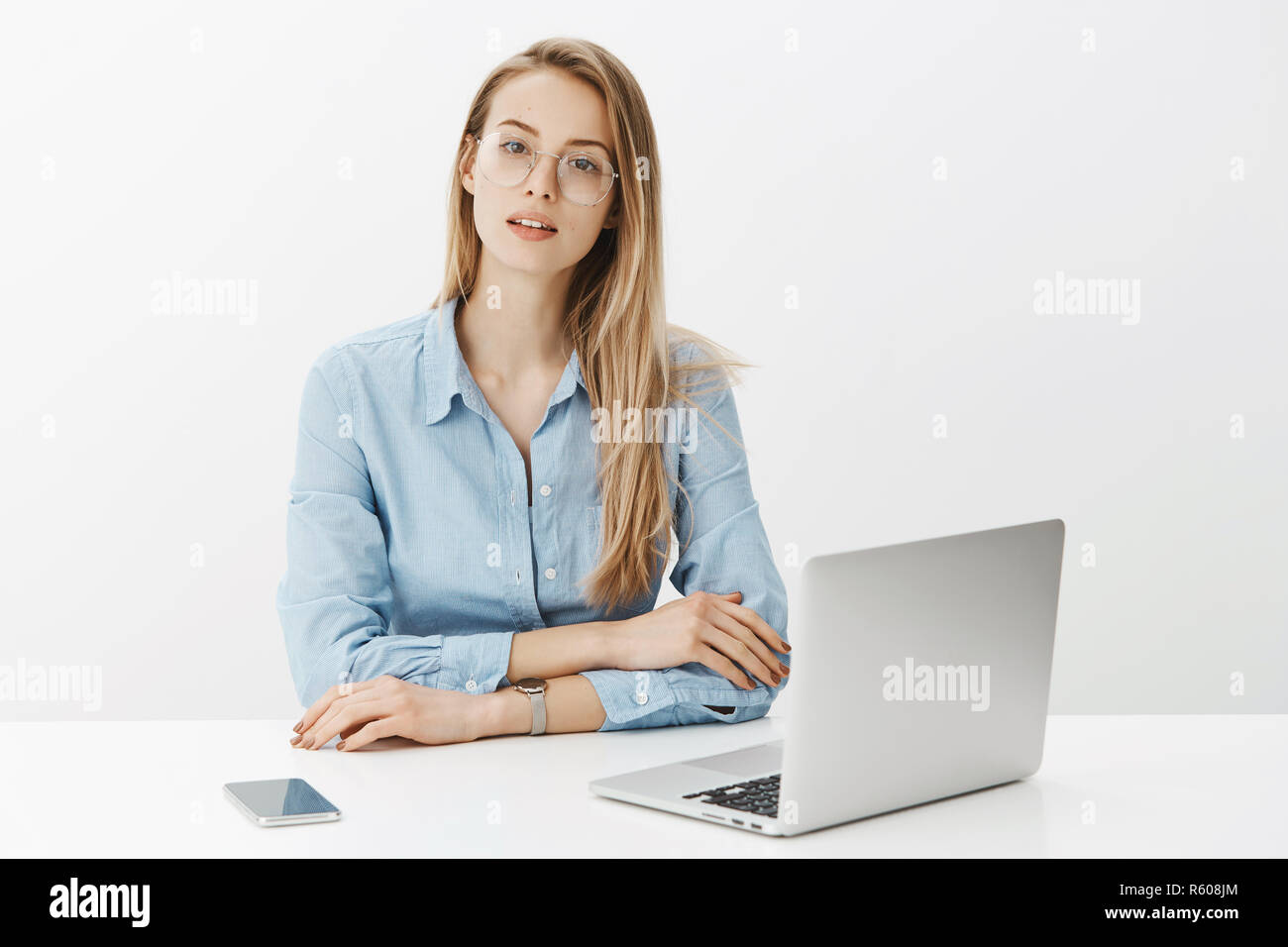 Hardworking smart and talanted female freelancer working hard on new project sitting near laptop and smartphone wearing glasses and watch looking at c Stock Photo
