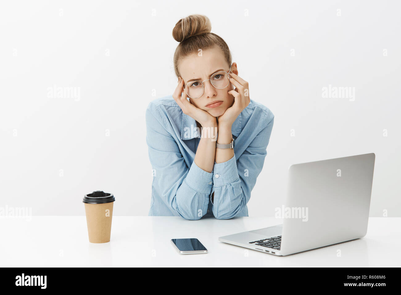 Sad and gloomy female coworker leaning head on hands and pouting with frown as feeling bored and tired working on article turning away from laptop as  Stock Photo
