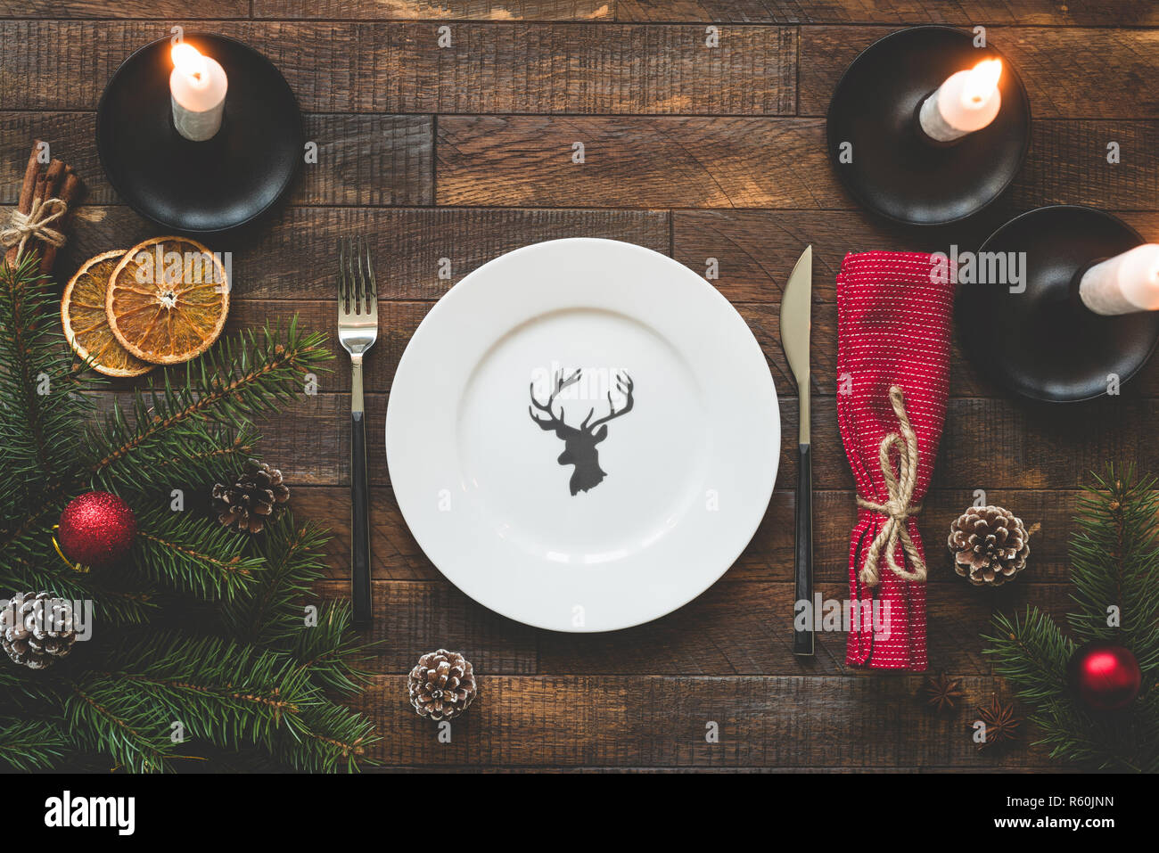 Christmas table setting with empty plate, silverware, burning candles, red table textile on rustic wooden table. Top view, copy space for text. Beauti Stock Photo