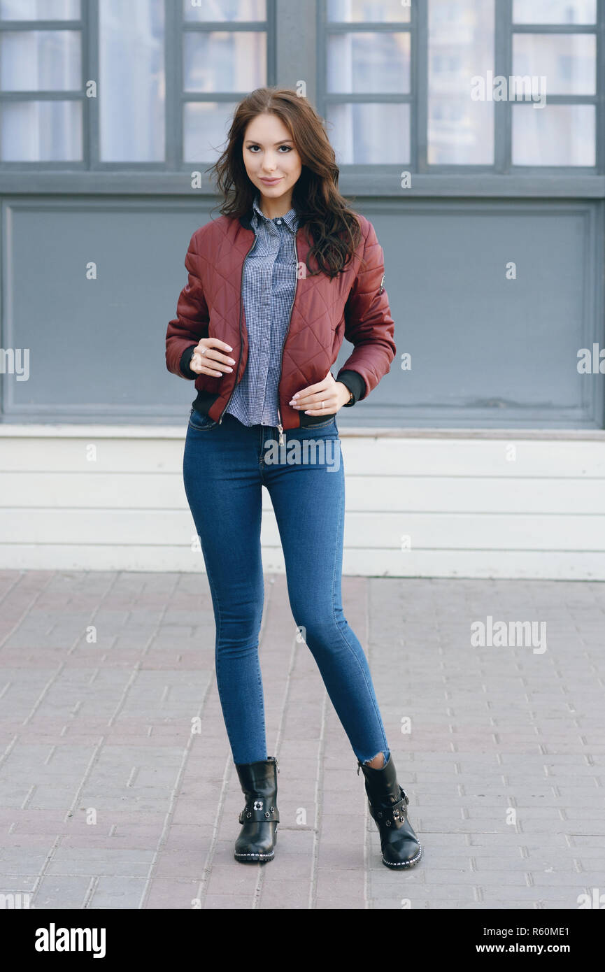 Young beautiful stylish woman in a burgundy pilot's jacket and blue jeans,  street style, spring and autumn trend, look, hair in the wind Stock Photo -  Alamy