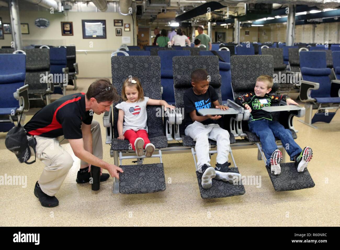 NORFOLK (April 27, 2017) Capt. Doug Casavant, master of the expeditionary fast transport ship USNS Spearhead (T-EPF-1), demonstrates the reclining function on one of the over 300 chairs in the passenger room during a tour of the ship during the command's 'Take Our Daughters and Sons to Work Day.' Stock Photo