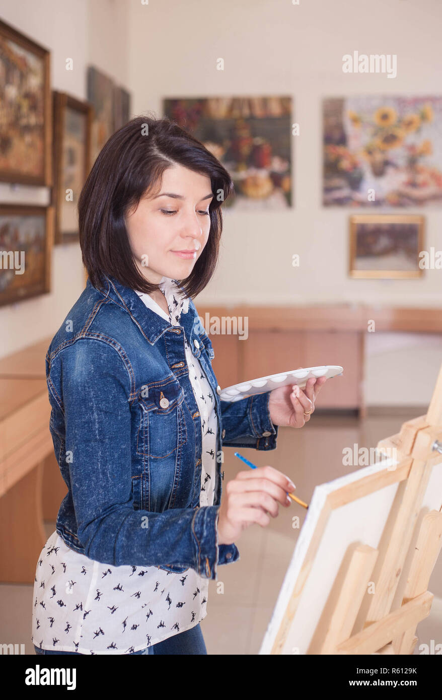 Cute young woman painting a picture near an easel in a creative studio ...