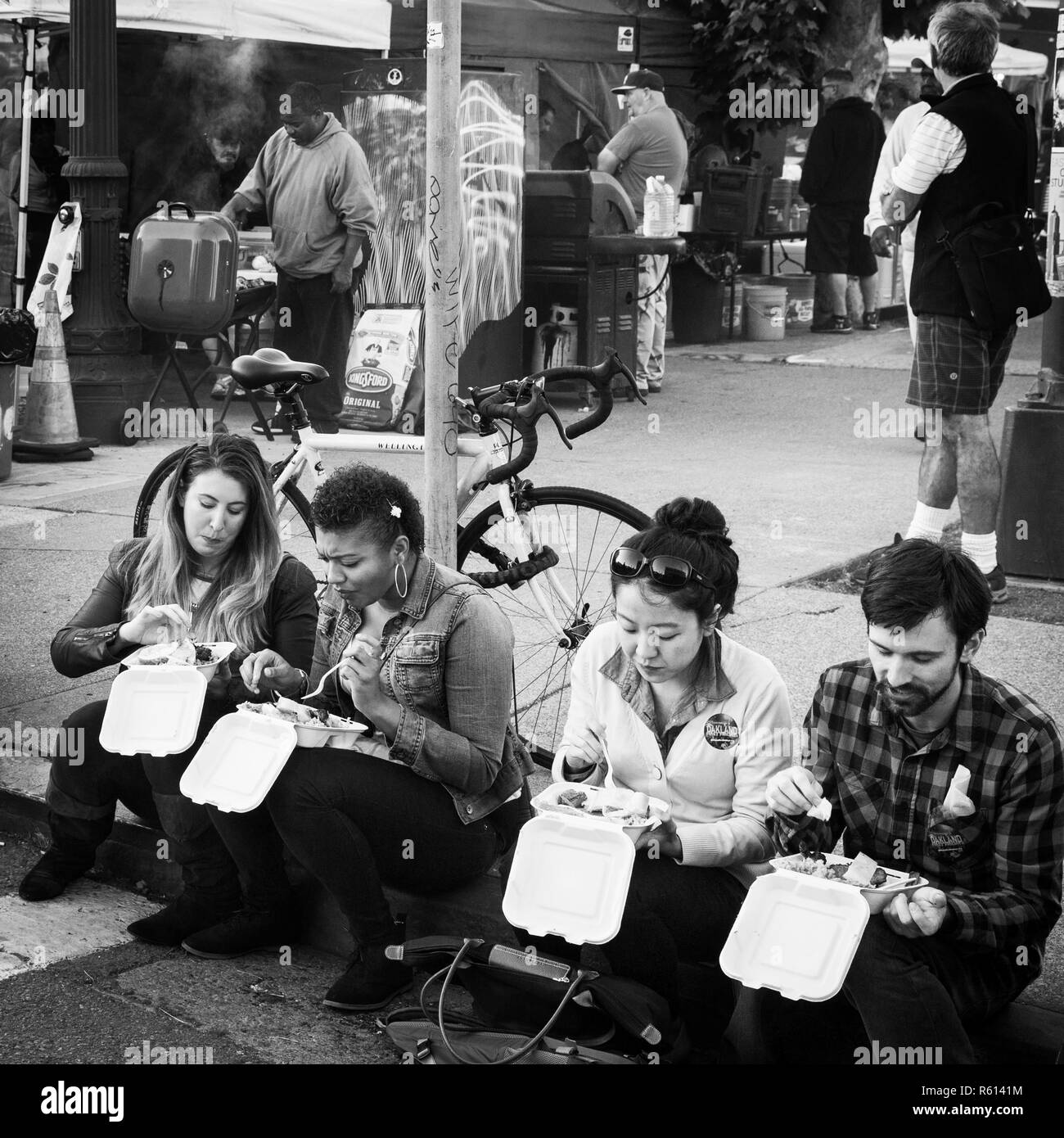 OAKLAND, CA-June 6, 2014: Millenials sit on the sidewalk curb eating street food at the city's monthly Art Murmur uptown gallery hop. Street chefs. Stock Photo