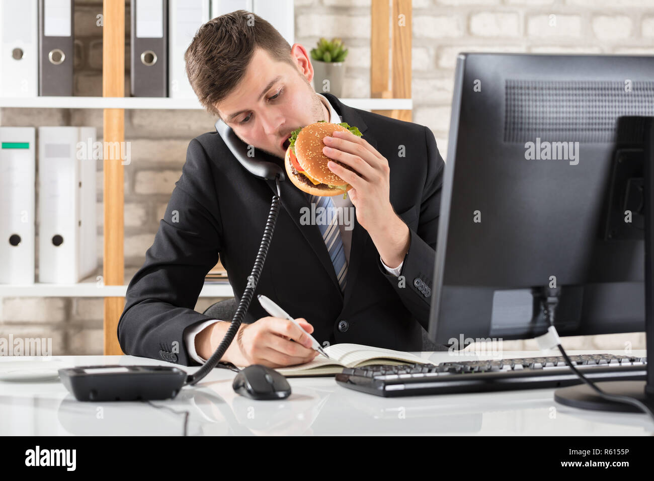 Business Man At Desk Eating Burger And Working Stock Photo