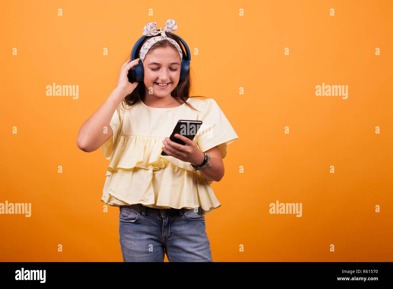 Little girl with yellow t-shirt listening music from her phone and headset. Joyfull gil Stock Photo