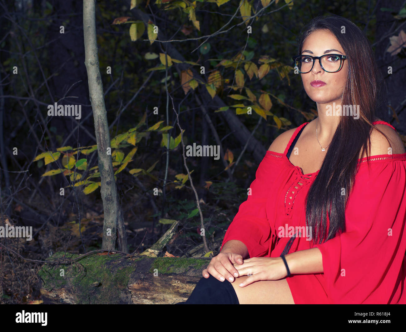 young women stiting in the forest wearing red dress and glasses Stock Photo