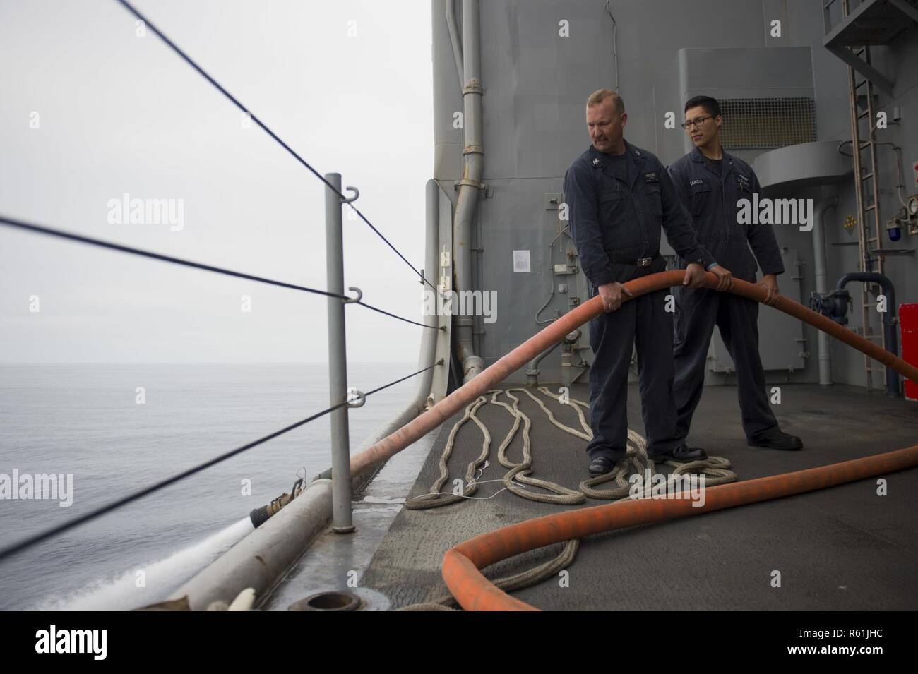PACIFIC OCEAN (May 4, 2017) Hull Technician 1st Class Jeff Kinard, a Boerne, Texas native, and Damage Control Fireman Jose Garcia, a Farmington, New Mexico native, both assigned to the engineering department of amphibious dock landing ship USS Pearl Harbor (LSD 52), drain a fire main off the ship’s boat deck. More than1,800 Sailors and 2,600 Marines assigned to the America Amphibious Ready Group (ARG) and the 15th Marine Expeditionary Unit (MEU) are currently conducting a Composite Unit Training Exercise (COMPTUEX) off the coast of Southern California in preparation for the ARG’s deployment la Stock Photo