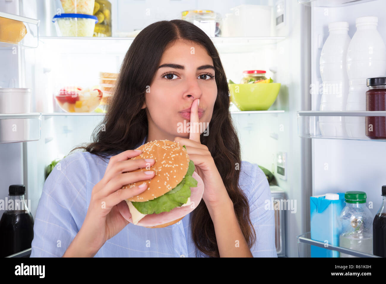 Woman Holding Burger With Finger On Lips Stock Photo