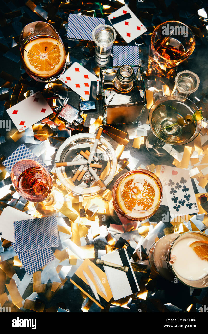 top view of cigarettes, alcoholic cocktails, playing cards, rolled banknote, credit cards and