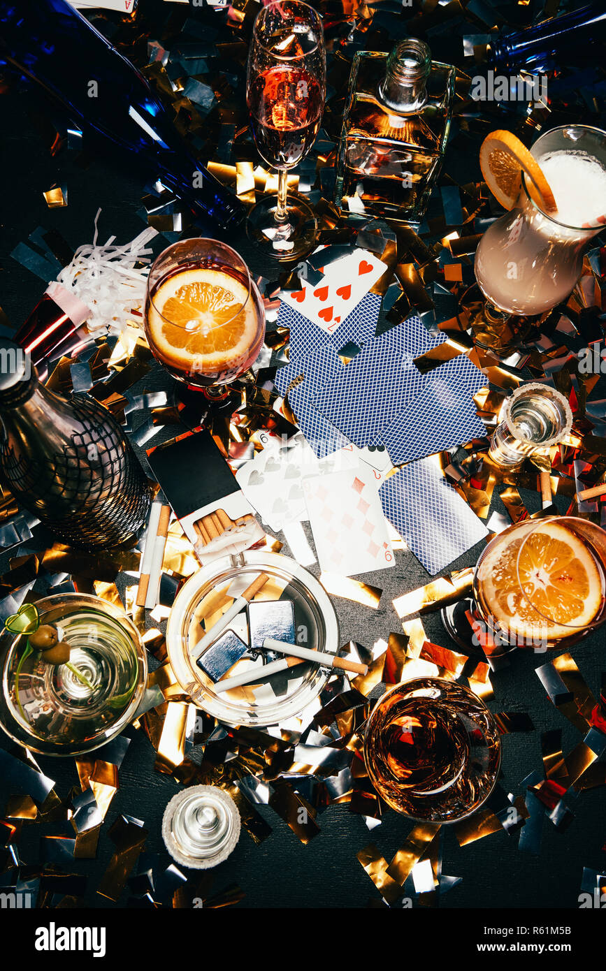 flat lay with cigarettes, alcoholic cocktails, whiskey and party horns on  table covered by golden confetti Stock Photo