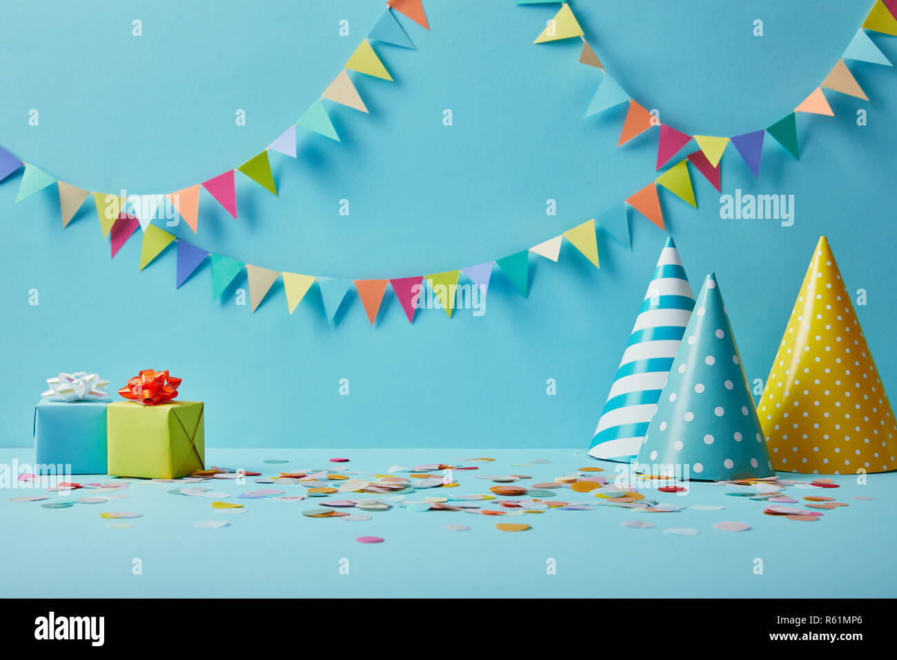 party hats, confetti and gifts on blue background with colorful bunting ...